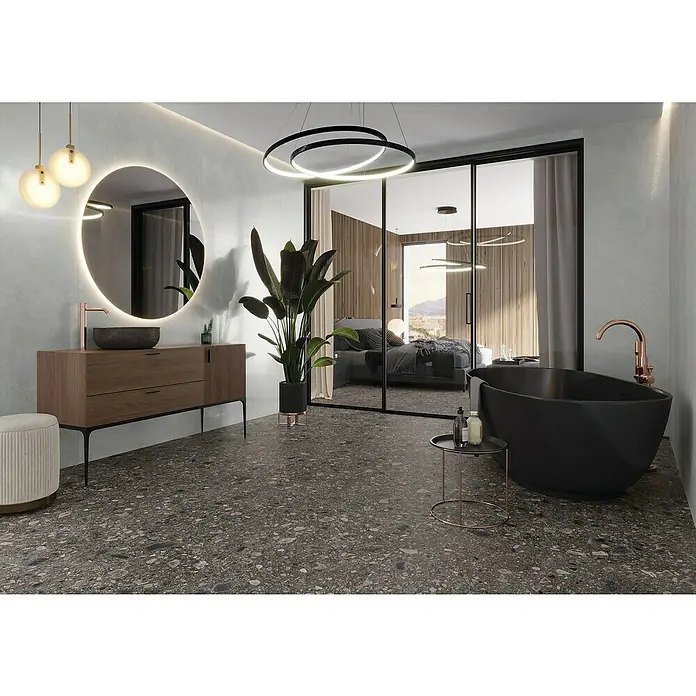 Feinsteinzeugfliese Terrazzo Ceppo - 59,7 x 59,7 cm, Schwarz, Matt - Ein modernes Badezimmer mit einem freistehenden schwarzen Bad, einem Waschtisch mit rundem Spiegel und Terrazzoboden, das ein luxuriöses Ambiente schafft.