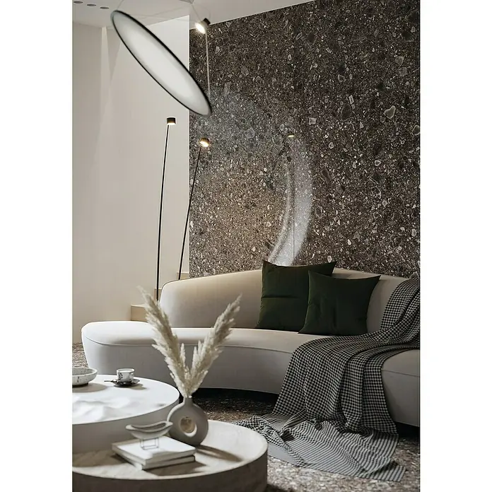 Feinsteinzeugfliese Terrazzo Ceppo - 119,7 x 119,7 cm, Schwarz, Glänzend - Elegantes Wohnzimmer mit beigem Sofa, dunklen Kissen, Couchtisch und auffälliger Beleuchtung, die eine moderne und stilvolle Atmosphäre schafft.