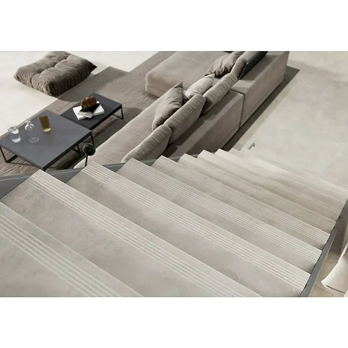 Queens Stufen- & Abdeckplatte - 29,8 x 119,8 cm, Weiß, Matt - Dieses Bild zeigt eine Treppe mit grauen Stufen im Vordergrund und einem Sofa und einem Tisch im Hintergrund.