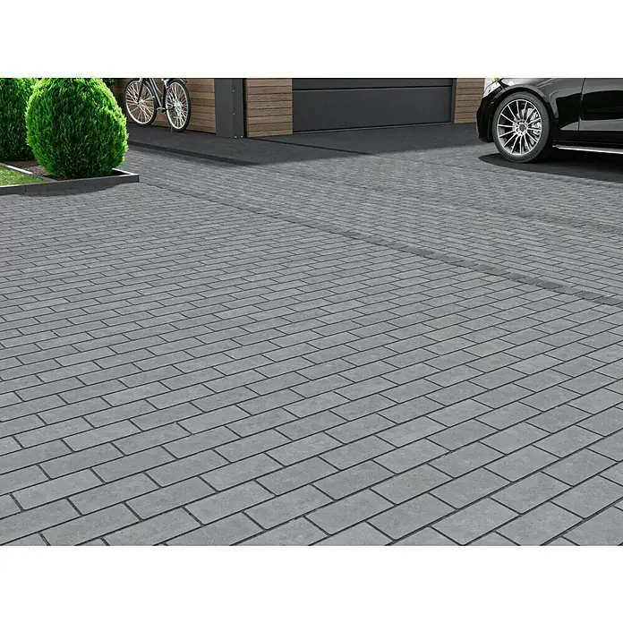 EHL Pflasterstein Drän - Anthrazit, 20 x 10 x 8 cm, Rechteckig - Graues Pflastersteinmuster, das eine breite, gepflasterte Auffahrt mit einem Auto, Fahrrädern und Büschen im Hintergrund zeigt.