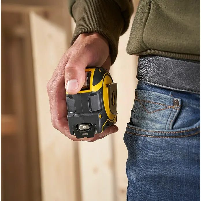 Stanley FatMax Kapselmaßband Autolock - Länge Maßband: 8 m - Nahaufnahme eines Mannes, der ein schwarzes und gelbes Maßband in der Hand hält, während er Arbeitskleidung trägt.