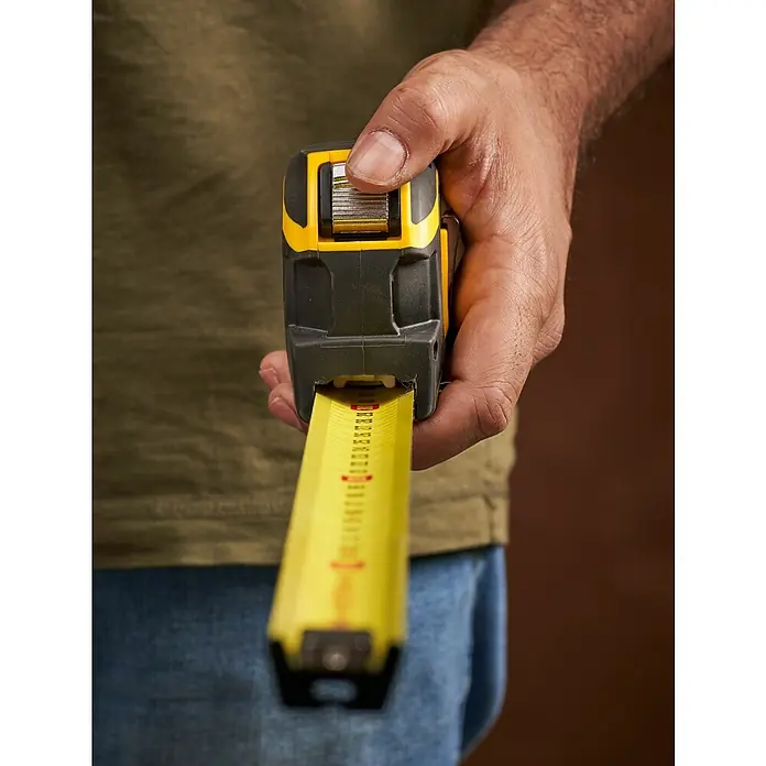 Stanley FatMax Kapselmaßband Autolock - Länge Maßband: 8 m - Nahaufnahme eines Mannes, der ein gelbes und schwarzes Rollmaßband hält, das Haltbarkeit und Präzision für Bauprojekte verspricht.