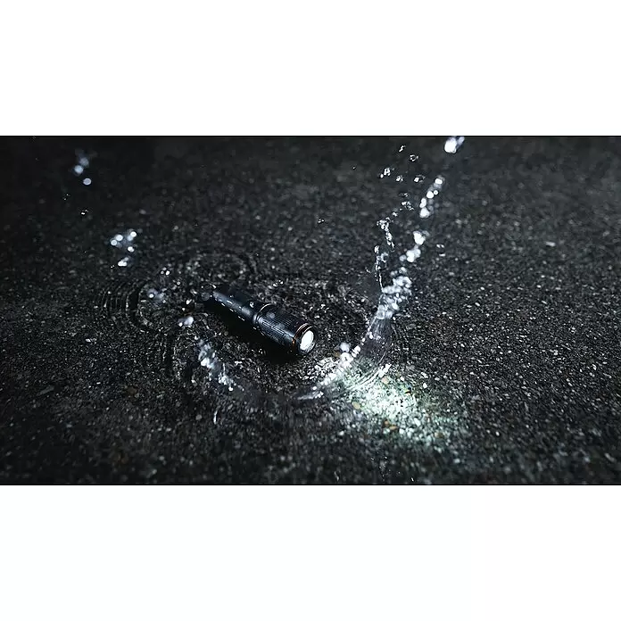 Nebo Tools Linterna Columbo - 100 lm - Linterna negra impermeable ilumina una superficie mojada con salpicaduras de agua.