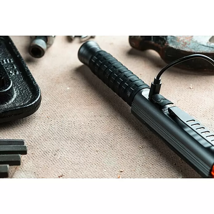 Nebo Tools Linterna Big Larry Pro+ - IPX7 - Linterna táctica negra con agarre texturizado y clip metálico, cargándose, rodeada de otras herramientas.