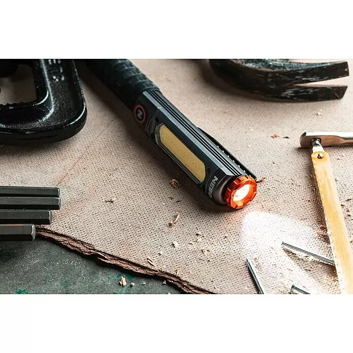 Nebo Tools Linterna Big Larry Pro+ - IPX7 - Linterna de trabajo NEBO negra con detalles naranjas, que ilumina un espacio con herramientas con su luz lateral y frontal.