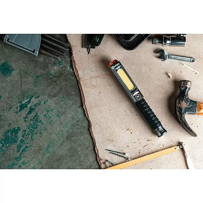 Nebo Tools Linterna Big Larry Pro+ - IPX7 - Linterna/luz de trabajo NEBO, negra con panel LED amarillo, rodeada de herramientas sobre una superficie texturizada.