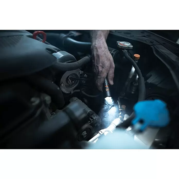 Nebo Tools Linterna Torchy 2K - 2.000 lm - Una mano sujeta una linterna negra con logo naranja, iluminando un motor de coche.