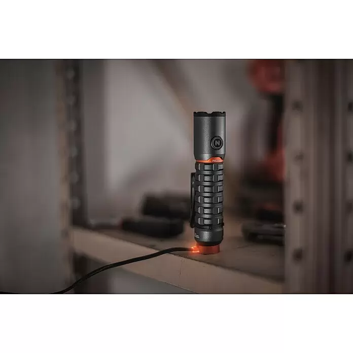 Nebo Tools Linterna Torchy 2K - 2.000 lm - Linterna gris oscuro y naranja cargando en un estante de madera en un taller.