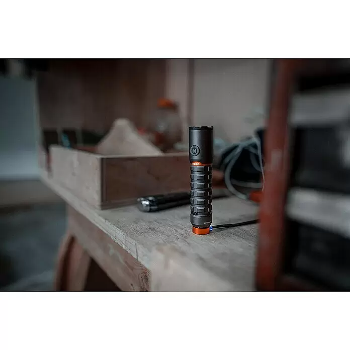 Nebo Tools Linterna Torchy 2K - 2.000 lm - Linterna gris oscuro y naranja sobre banco de trabajo de madera, cargando con luz azul en la base.