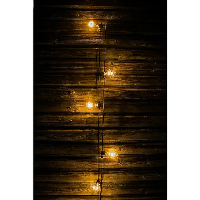 Konstsmide LED-Lichterkette - Außen, 5 m, Lichtfarbe: Warmweiß, Batteriebetrieben - Fünf Glühbirnen an einer Schnur beleuchten eine rustikale Holzwand und erzeugen ein warmes, einladendes Ambiente.