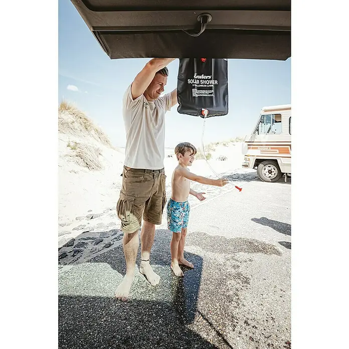 Enders Solardusche - 20 l - Ein Mann und sein Sohn benutzen eine tragbare Solardusche der Marke Enders im Freien. Die Dusche hängt an einem Fahrzeug.