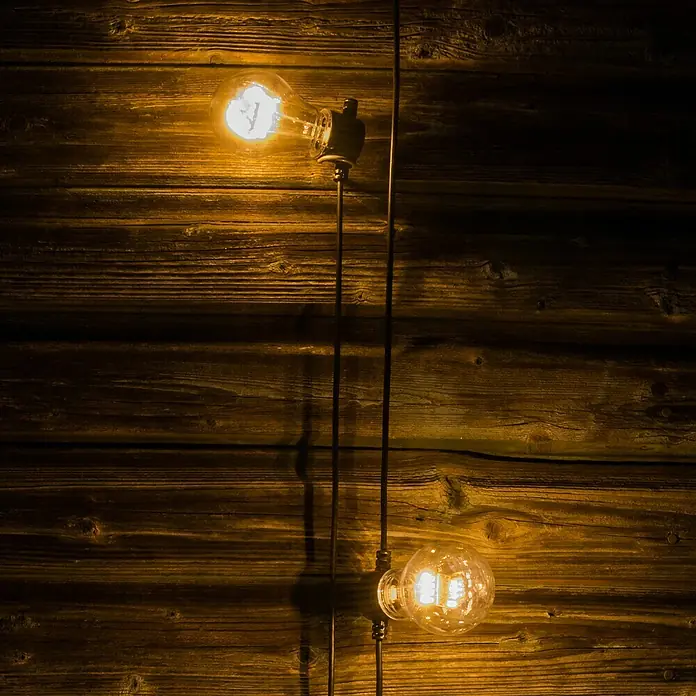 Konstsmide LED-Lichterkette - Außen, 5 m, Lichtfarbe: Warmweiß, Batteriebetrieben - Zwei Edison-Glühbirnen an einer Holzwand. Das warme Licht der Lampen erzeugt eine gemütliche Atmosphäre in dem rustikalen Raum.