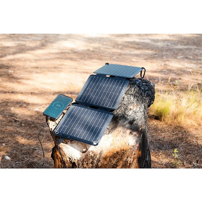 Panel solar plegable Innovate - 21 W, 2 conexiones USB - Un panel solar plegable carga un teléfono inteligente sobre un tronco de árbol. Ideal para actividades al aire libre y energía sostenible.