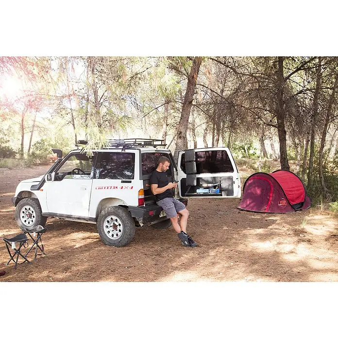 Panel solar plegable Innovate - 21 W, 2 conexiones USB - Un SUV blanco con equipo de camping, incluyendo una tienda y una cocina, en un entorno boscoso.