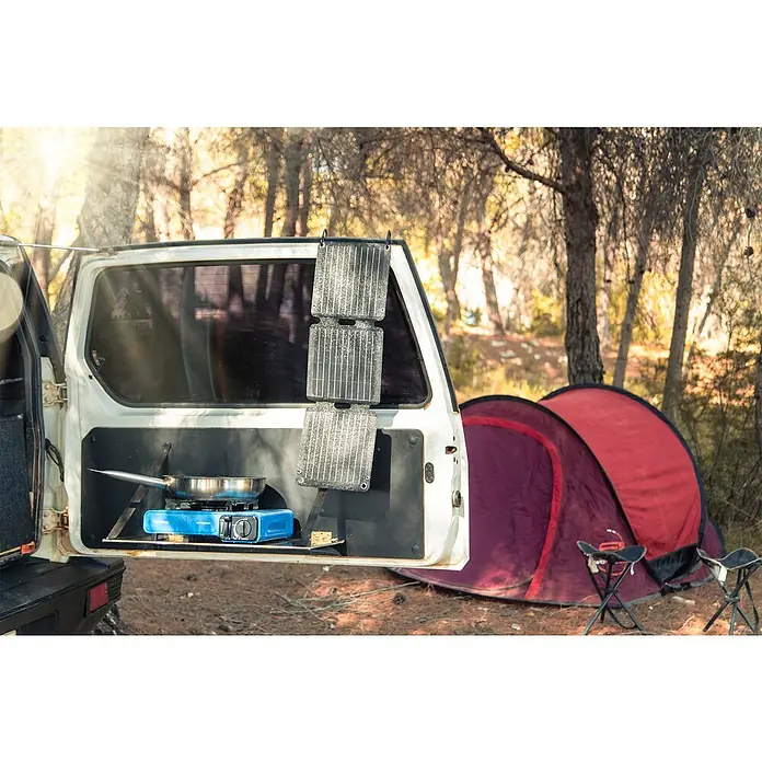 Panel solar plegable Innovate - 21 W, 2 conexiones USB - Configuración de camping con área de cocina en el portón trasero, cocina portátil, paneles solares y una tienda de campaña al fondo para aventuras al aire libre.