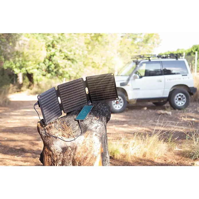 Panel solar plegable Innovate - 21 W, 2 conexiones USB - La estación de carga de paneles solares plegable con USB está alimentando un teléfono inteligente al aire libre. Ideal para acampar y aventuras.