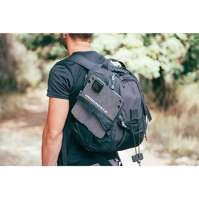 Panel solar plegable Innovate - 21 W, 2 conexiones USB - Primer plano de una mochila negra con un panel solar Innovate acoplado. Ideal para aventuras al aire libre y carga ecológica.