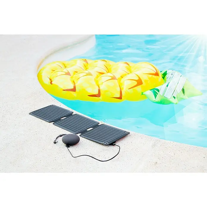 Panel solar plegable Innovate - 21 W, 2 conexiones USB - El cargador de panel solar portátil junto a una piscina con un flotador de piña en el fondo. Ideal para actividades al aire libre.