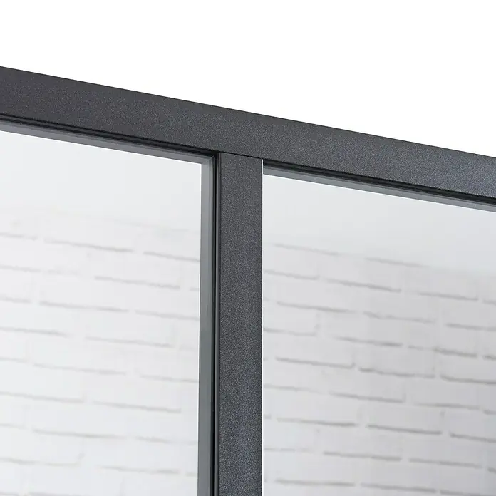 Kit atelier Glastrennwand Loft Bistro1.232 x 1.200 mm, Einscheibensicherheitsglas (ESG) - Nahaufnahme einer modernen schwarzen Glastür mit minimalistischem Design und Blick auf eine weiße Ziegelwand. Das Glas der Tür ist klar und reflektierend.