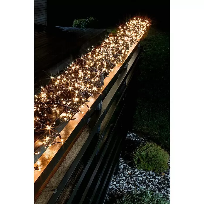 Konstsmide LED-Clusterlichterkette Micro LED Cluster - Außen, Länge: 9,3 m, 576 Stk., Netzbetrieben, Lichtfarbe: Bernstein - Warmweiße LED-Lichterkette auf einer dunklen Holzreling, schafft festliche Nachtbeleuchtung.