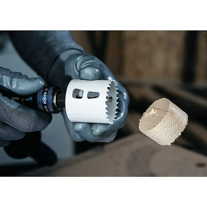 Bosch Professional Sierra de corona BiM - Diámetro: 73 mm, Acero - Una foto de cerca de una sierra de corona blanca de Bosch que se utiliza con un adaptador, junto a un núcleo de madera que se acaba de cortar.