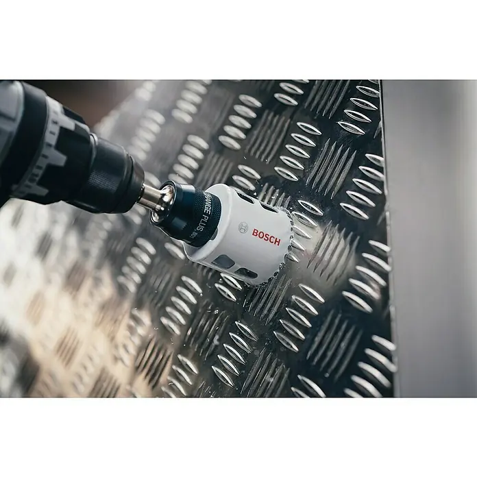 Bosch Professional Sierra de corona BiM - Diámetro: 73 mm, Acero - Primer plano de una sierra de corona Bosch perforando una superficie metálica texturizada, destacando precisión y potencia.