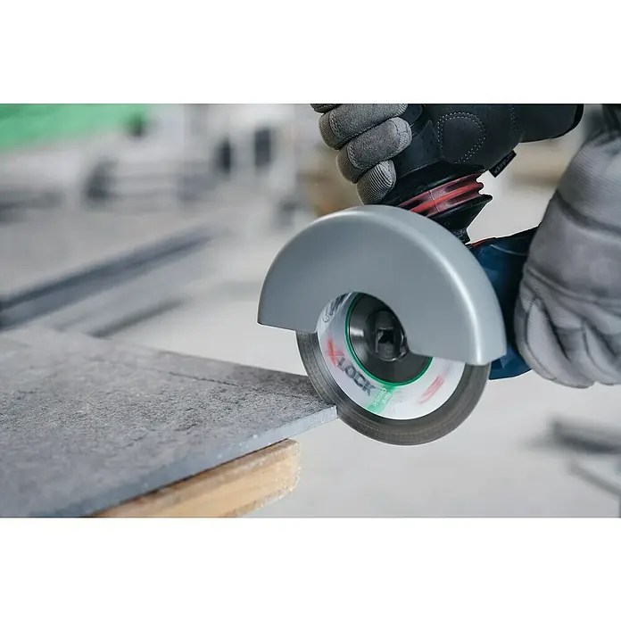 Bosch Professional X-Lock Diamant-Trennscheibe Standard for Ceramic - Durchmesser Scheibe: 125 mm, Geeignet für: Keramik - Eine Fliese wird mit einem Winkelschleifer mit X-LOCK-System bearbeitet, Schutzhandschuhe sind zu sehen.