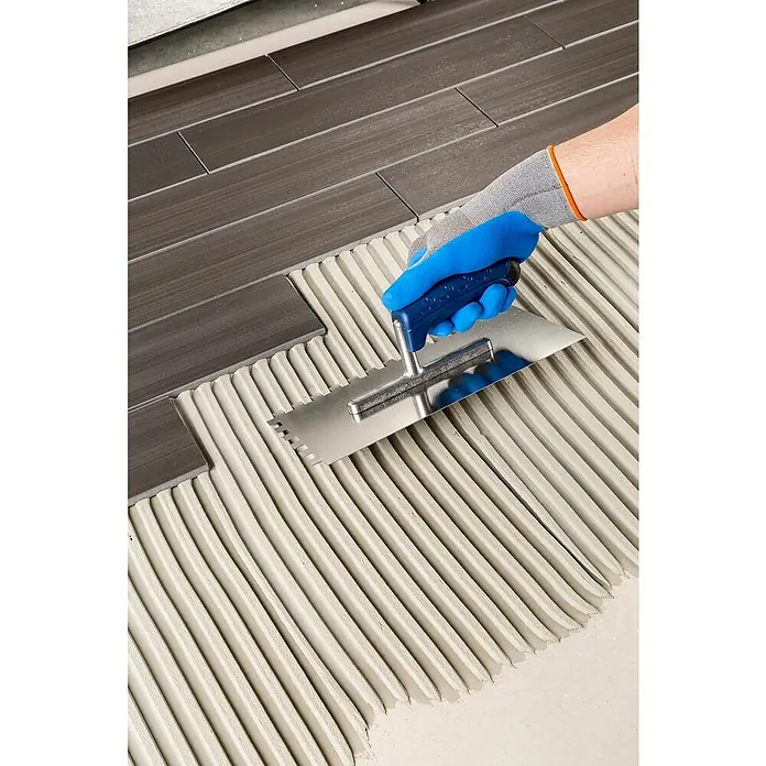 Knauf Flexkleber Extra - 20 kg - Bild einer gezackten Fliesenkelle, die zum Auftragen von Kleber für die Verlegung von Fliesen verwendet wird. Das Werkzeug ist ideal für Heimwerker.