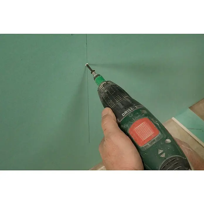Knauf TOP 2000 Verbundplatte EPS - 1.250 x 900 x 33 mm - Bohrmaschine verschraubt eine Schraube in eine grüne Wand. Das Werkzeug ist eine handliche Bohrmaschine mit rotem Knopf, die Schrauben präzise anbringt.