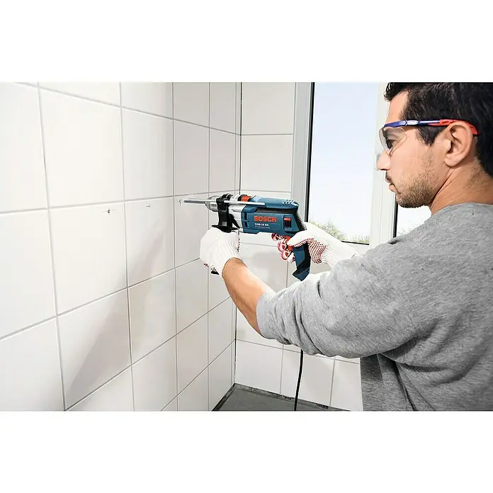 Bosch Fliesenbohrer CYL-9 - Durchmesser Bohrer: 6 mm - Mann bohrt mit einer Bosch GSB 16 RE Schlagbohrmaschine Löcher in eine geflieste Wand. Sicheres Arbeiten mit Schutzbrille und Handschuhen.