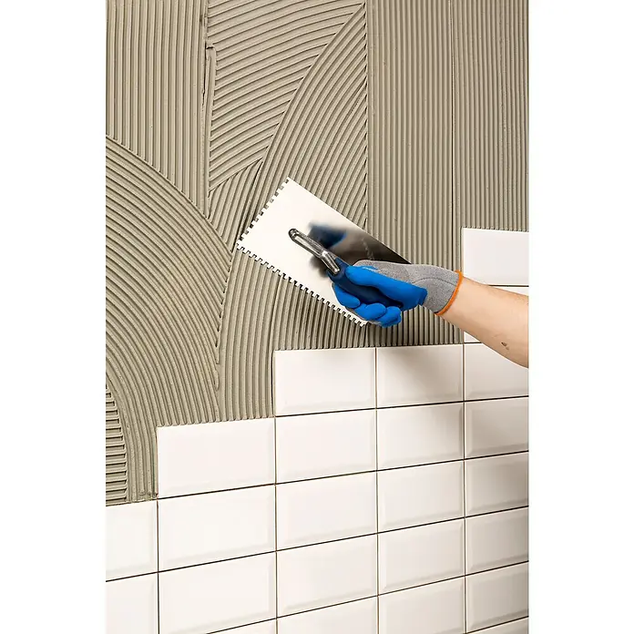 Knauf Flexkleber Extra - 20 kg - Auftragen von Klebstoff für weiße U-Bahn-Fliesen mit einer rostfreien Kelle. Die Fliesen werden an eine Wand geklebt.