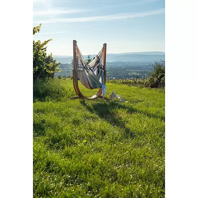 La Siesta Hängematten-Set Udine - L x B x H: 180 x 115 x 163 cm, Grau/Blau/Beige - Gestreifte Hängematte auf Holzgestell, mit Getränken auf einem Grashügel, mit Blick auf ein Tal.
