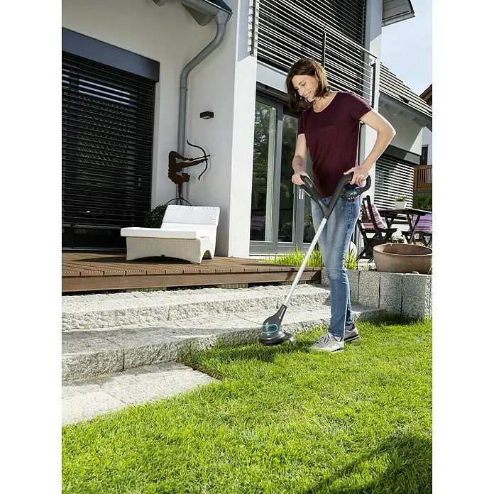 Gardena SmallCut Akku-Rasentrimmer Li-23 R - 14,4 V, 2 Ah, Li-Ionen, 1 Akku, Schnittbreite Messer: 22,3 cm - Eine Frau benutzt einen GARDENA Akku-Rasentrimmer EasyCut 23/18V P4A, um den Rasen zu trimmen. Das Gerät ist leicht und handlich.