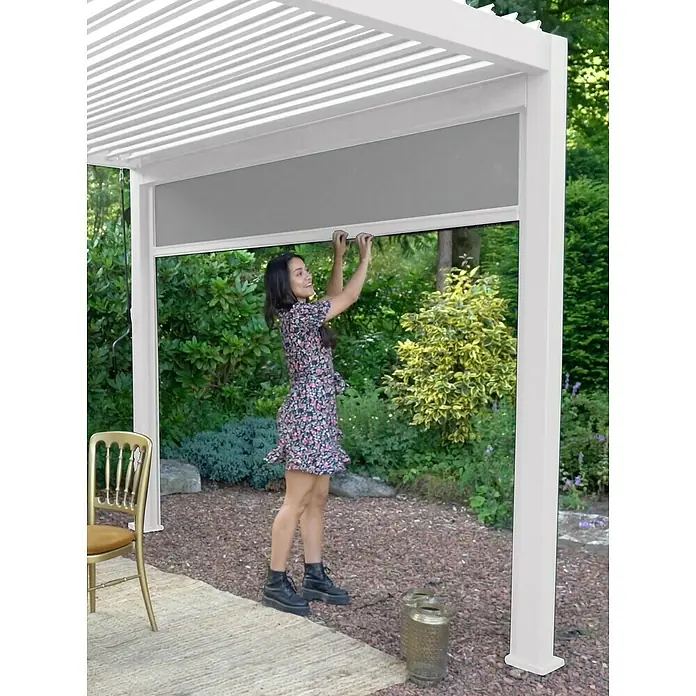 Sorara Seitenelement Rollo Solid & Basic - 400 cm, Weiß - Eine Frau bedient eine stilvolle, weiße Pergola mit einem praktischen Rollo für zusätzlichen Schatten und Privatsphäre im Garten.