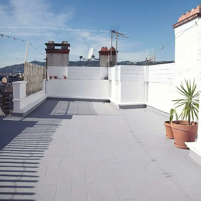 Soprema Impermeabilizante Campolin Fiber - Gris, 20 kg - Terraza plana con baldosas grises, rodeada por una pared blanca. Dos macetas de terracota con plantas verdes se ubican al lado.