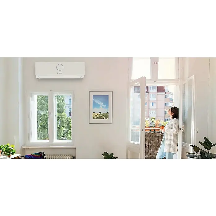 Bosch Aire acondicionado Inverter Climate 3000 i - 2.600 W, 2.900 W, 18 m², Blanco - Moderno aire acondicionado de Bosch en la pared de un salón luminoso, garantizando una refrigeración agradable y un ambiente elegante.