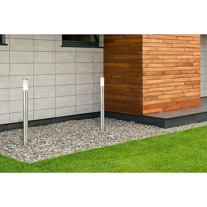 Globo Boston Lámpara de pie para exterior - 60 W, Color del marco: Plateado, 12,7 x 12,7 x 110 cm, Sin bombillas - Iluminación exterior moderna: dos balizas plateadas iluminan un camino de grava frente a una fachada con elementos de madera y césped.