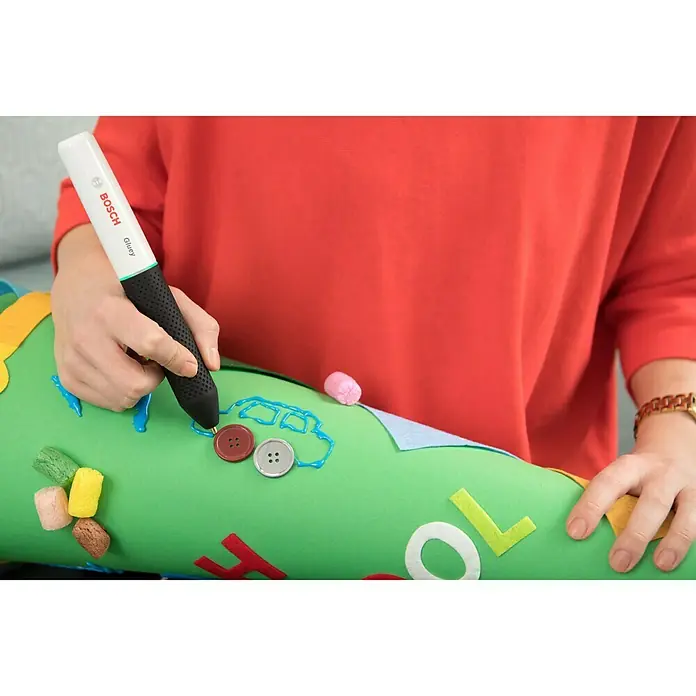 Bosch Akku-Heißklebestift Gluey - Farbe: Marshmallow - Nahaufnahme von einer Person, die mit dem Bosch Gluey Klebestift auf einer grünen Oberfläche bastelt.