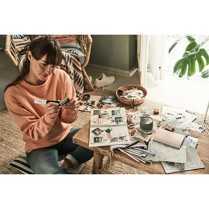 Bosch Akku-Heißklebestift Gluey - Farbe: Smoky Grey - Frau sitzt mit Bosch Klebestift am Tisch und bastelt an einem Scrapbook.