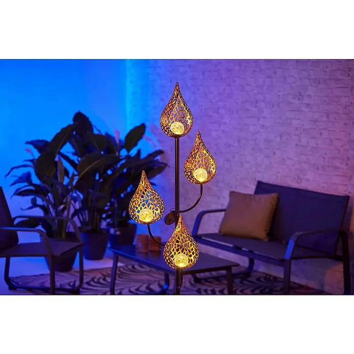 BAUHAUS Solar-Erdspieß Flame - 0,06 W, L x B x H: 38 x 38 x 151 cm, Schwarz/Gold, IP44 - Eine stimmungsvolle Szene mit einer dekorativen Gartenleuchte, die warmes Licht durch ihre filigranen Muster wirft.