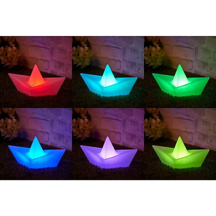 BAUHAUS Solar-Dekoleuchte Schiff - Weiß, IP65 - Sechs leuchtende Papierboot-Lampen in Rot, Cyan, Grün, Blau, Violett und Limettengrün auf einem Rasen vor einer Mauer.