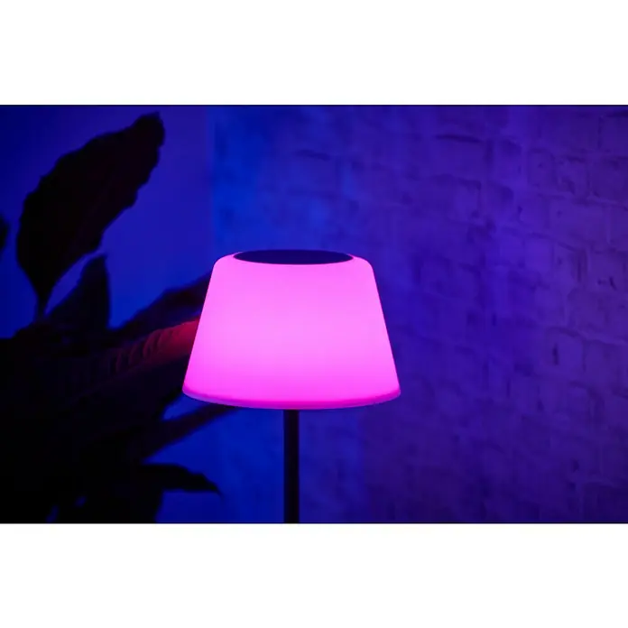 BAUHAUS Solar-Stehleuchte - 5,8 W, L x B x H: 27,5 x 27,5 x 105,5 cm, Schwarz/Weiß, IP44 - Nahaufnahme einer modernen, pinkfarbenen Tischlampe mit stimmungsvoller Beleuchtung vor einer Backsteinwand und einer Pflanze im Hintergrund.