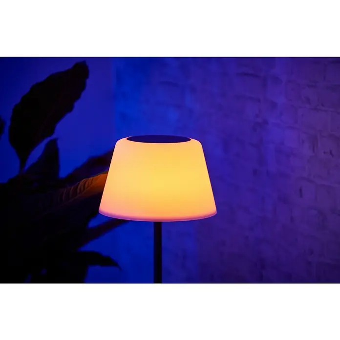 BAUHAUS Solar-Stehleuchte - 5,8 W, L x B x H: 27,5 x 27,5 x 105,5 cm, Schwarz/Weiß, IP44 - Tischleuchte mit warmem, gelbem Licht und dunklem Sockel vor einer blauen Backsteinmauer. Das Design ist modern und schlicht.