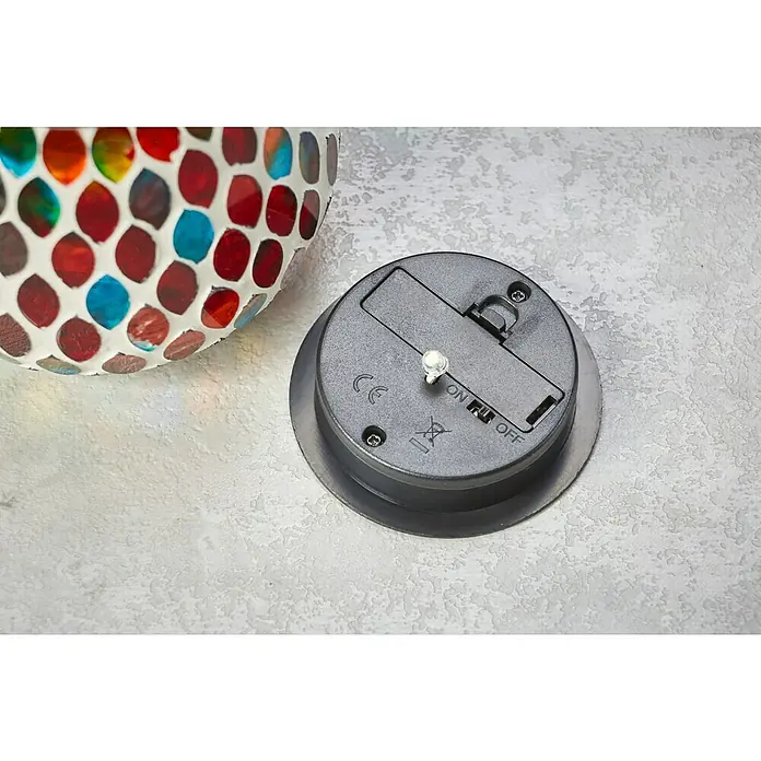 BAUHAUS Solar-Tischleuchte - L x B x H: 14,5 x 10,5 x 10,5 cm, Bunt, 0,06 W, IP44 - Nahaufnahme eines Solarlichts mit Mosaikmuster und Schalter auf der Rückseite. Das Licht ist ausgeschaltet und hat eine runde Basis.