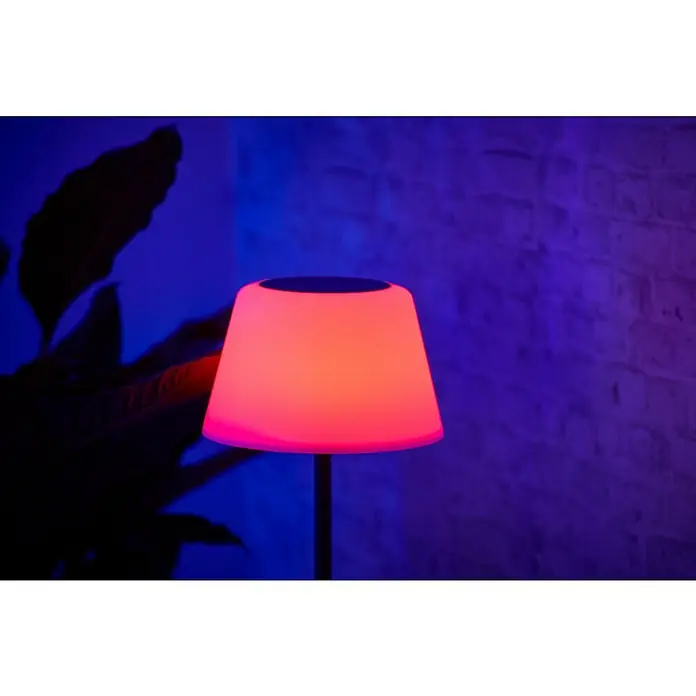 BAUHAUS Solar-Stehleuchte - 5,8 W, L x B x H: 27,5 x 27,5 x 105,5 cm, Schwarz/Weiß, IP44 - Nahaufnahme einer beleuchteten Tischlampe mit rotem Schirm, die eine gemütliche Atmosphäre in einem dunklen Raum mit Ziegelwand schafft.