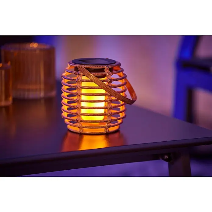BAUHAUS Solar-Tischleuchte - Rattan, IP44 - Nahaufnahme einer dekorativen Solar-Laterne aus Rattan mit warmem Lichtschein auf einem Tisch, die eine gemütliche Atmosphäre erzeugt.