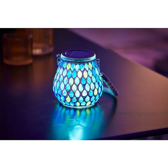 BAUHAUS Solar-TischleuchteL x B x H: 14,5 x 10,5 x 10,5 cm, Blau, IP44 - Schönes Bild einer blauen Mosaik-Solarleuchte mit Henkel auf einem Tisch, die ein warmes Licht ausstrahlt und eine gemütliche Atmosphäre schafft.