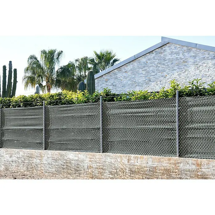Faura Malla de ocultación 120 - 10 x 1,5 m, Antracita - Una valla metálica gris con pantalla de privacidad se encuentra frente a una casa revestida de piedra y palmeras, ofreciendo privacidad y seguridad.
