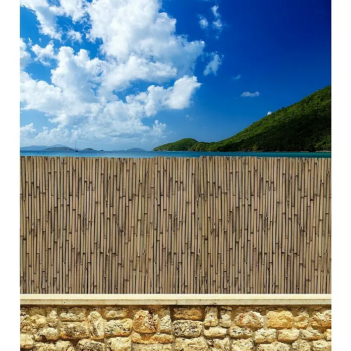 Faura Ocultación de bambú barnizado - L x Al: 3 x 1,5 m, Marrón - Una valla de bambú frente a un paisaje costero con cielo azul y nubes. La valla es el elemento principal de la imagen.