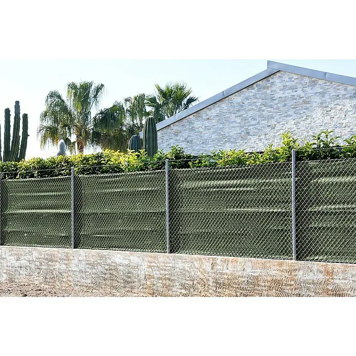 Faura Malla de ocultación 90 Extra - 10 x 2 m, Verde - Primer plano de una cerca de tela metálica verde que brinda privacidad, con exuberante vegetación y cactus al fondo.